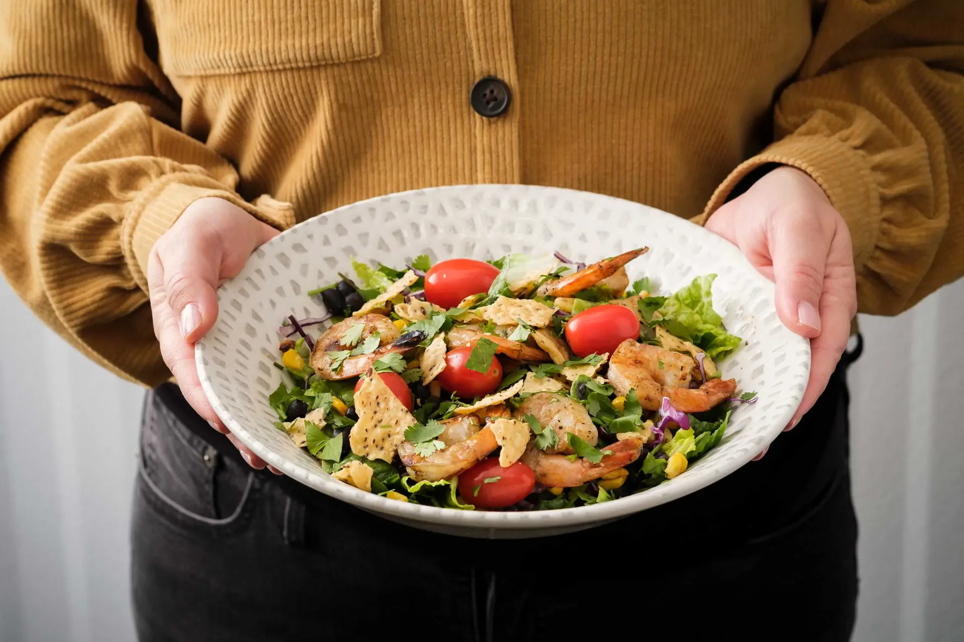 Hands holding bowl of salad with shrimp and assorted toppings