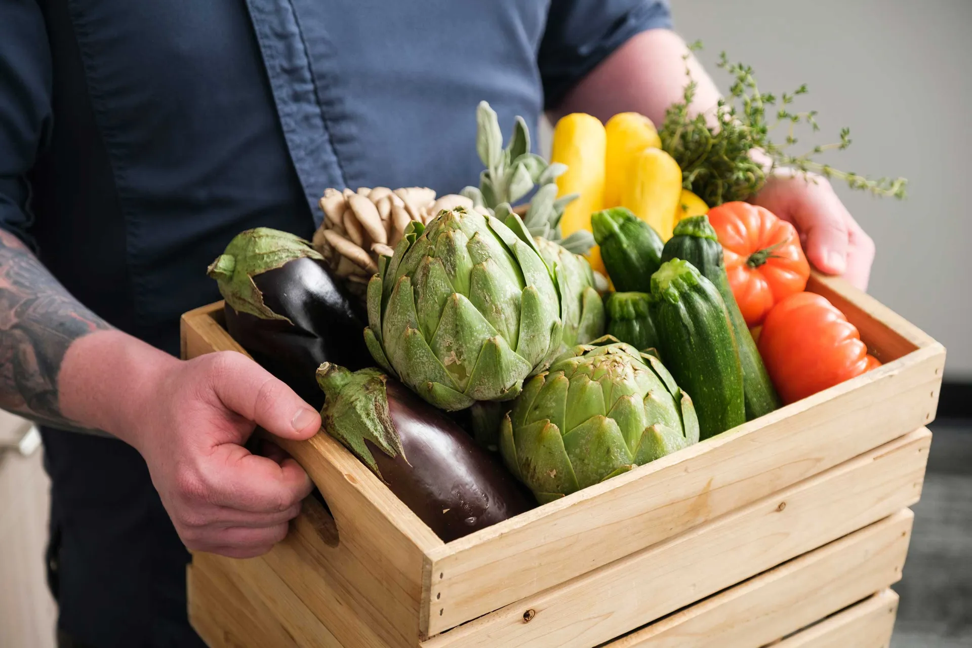 Hands holding wooden crate of assorted vegetables