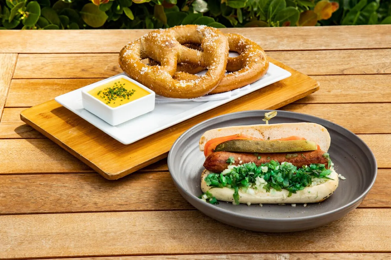 A Chicago Dog and fresh baked soft pretzel with mustard set atop a wooden slat table