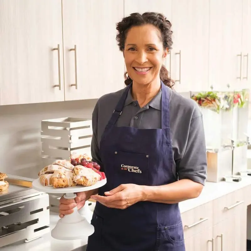 Server smiling while holding a platter of fresh scones in front of catered buffet