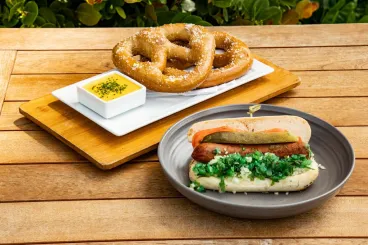 A Chicago Dog and fresh baked soft pretzel with mustard set atop a wooden slat table