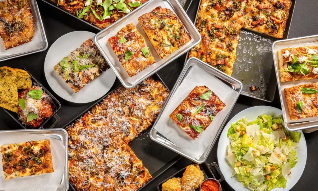 Overhead view of assorted grandma style pizza, garlic knots and caesar salad