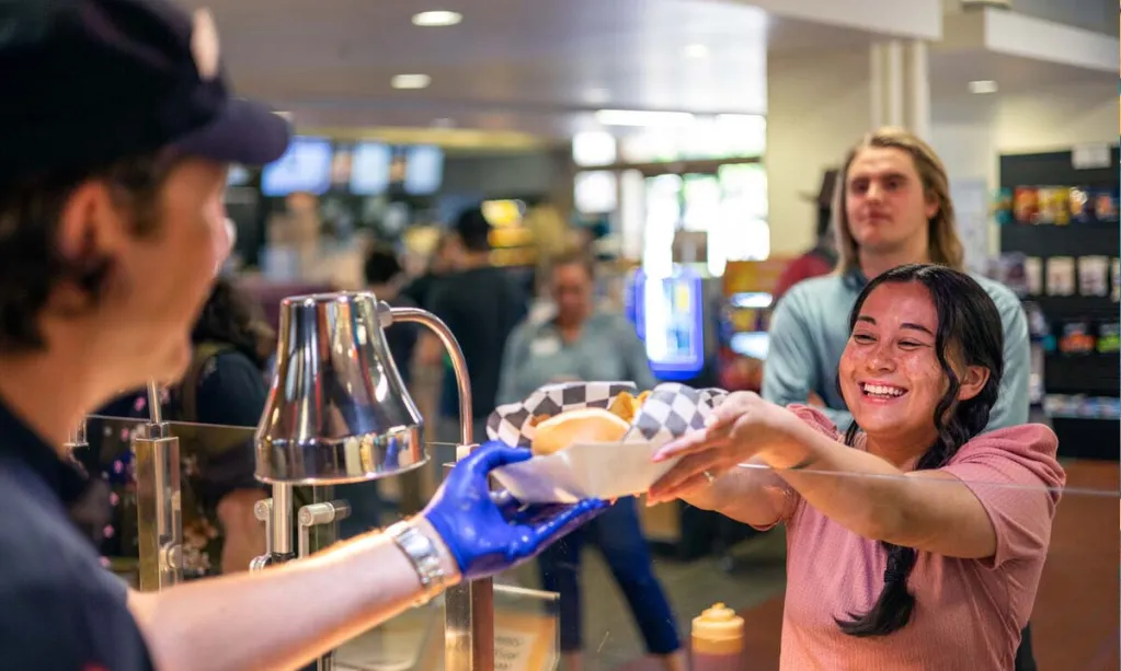 Person smiling while grabbing food from server in cafeteria