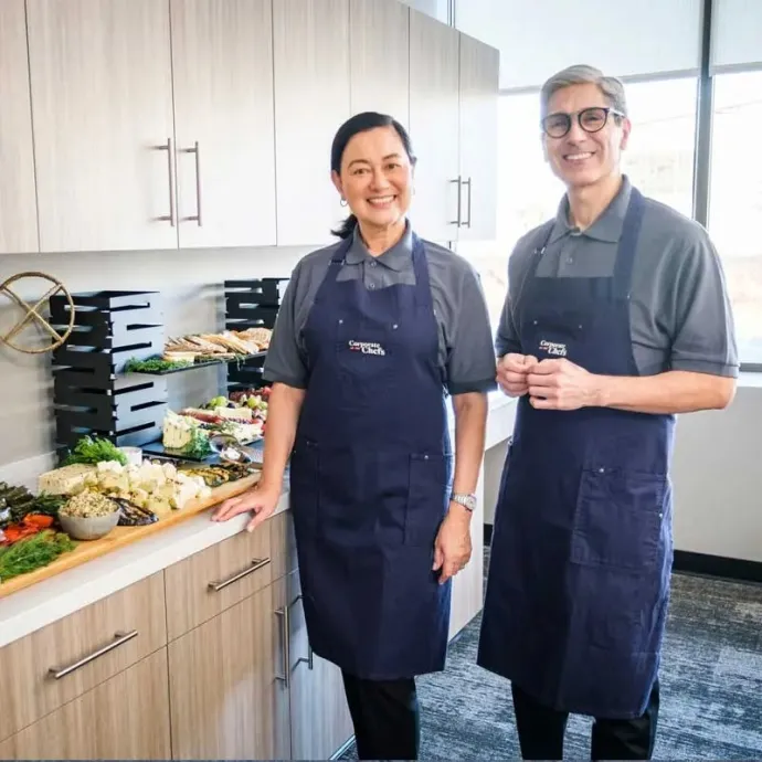 Two catering attendents smiling while standing in front of charcuterie board