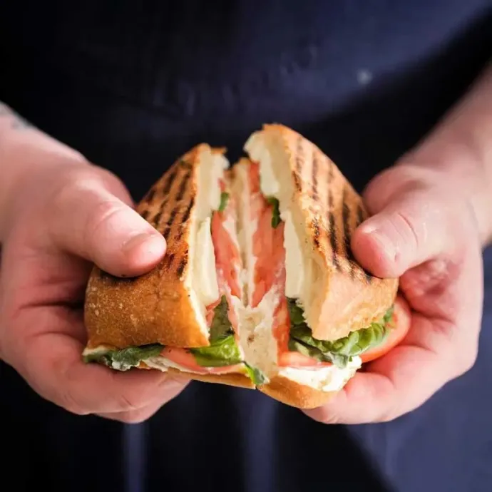 Hand holding and opening a freshly grilled caprese panini